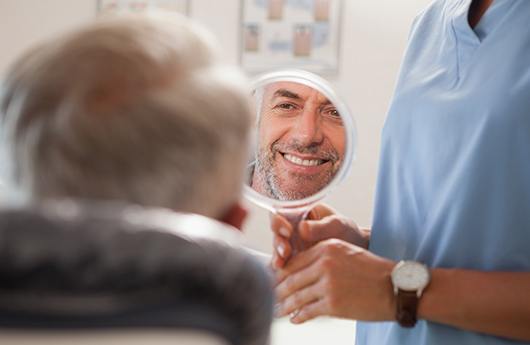Man looking in mirror during smile makeover appointment