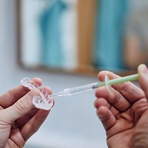 Hands holding a teeth whitening tray and some bleaching gel