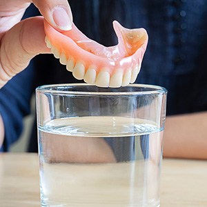 person putting dentures in water