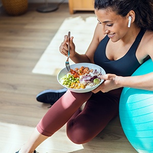 Woman eating salad in workout clothes leaning on medicine ball