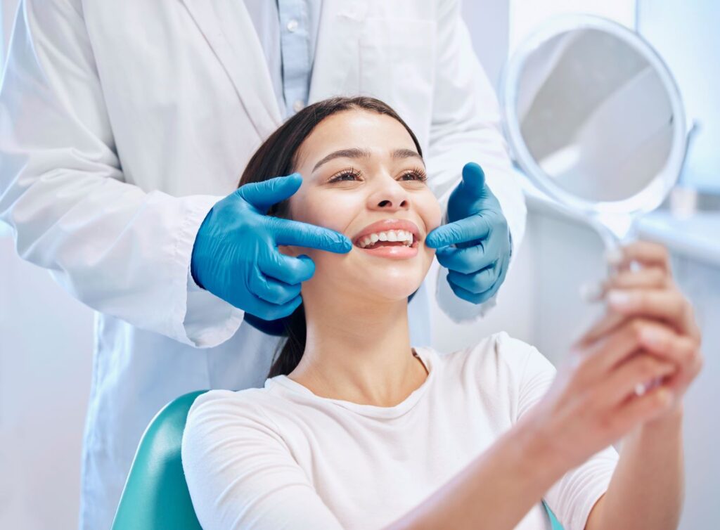 A woman smiling in a hand mirror at the dentist.